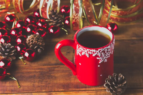 Red cup of tea and Christmas balls on wooden background — Stock Photo, Image