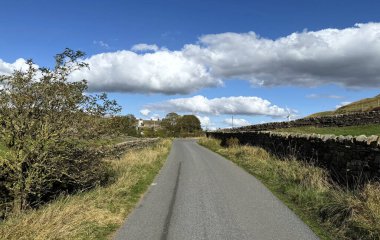 Jowett Yolu, parlak mavi sonbahar gökyüzünün altına kadar uzanıyor. Yumuşak beyaz bulutlar ve çevreleyen alanlar Silsden, Yorkshire, İngiltere yakınlarında sakin bir atmosfer yaratıyor.