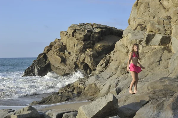 Una chica en traje de baño rosa en la playa rocosa . — Foto de Stock