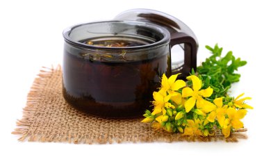 Glass cup with herbal tea and blooming Johns wort flowers on burlap mat, isolated on white background, natural medicine and healing herbs concept