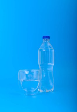 Açık mavi arka planda plastik şişe ve bir bardak temiz su, saflık, su, tazelik ve sağlıklı yaşam konsepti.