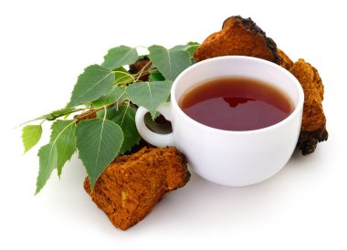 Bir fincan mayalanmış mantar çayı, huş yaprakları ve beyaz arka planda izole edilmiş kurutulmuş chaga parçaları.