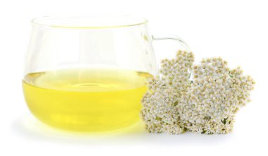 Beyaz bir zemin üzerinde izole edilmiş, bir yığın taze beyaz kiraz çiçeği (Achillea millefolium) yanında sarı bitkisel çayla dolu cam bardak. Doğal tıp ve sağlığı temsil eder..