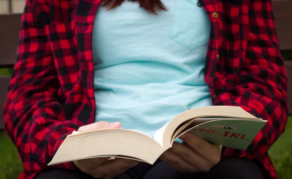 Ganska ung flicka läsa en bok och sitta på bänken i den — Stockfoto