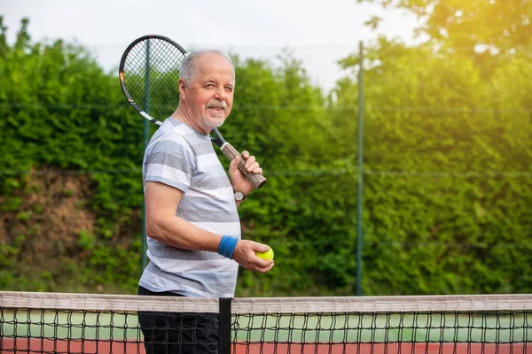 Leende, sportig, aktiv senior man spelar tennis utomhus, sport pensionär, sport koncept — Stockfoto