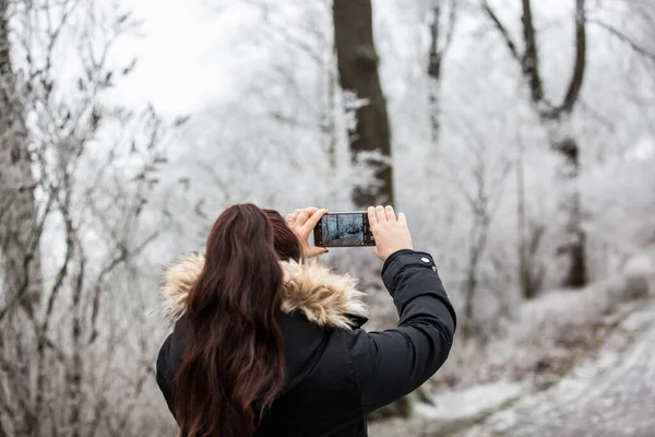 Söt ung brunett kvinna tar bild av en frusen skog vid den mobila durig härlig vintertid — Stockfoto