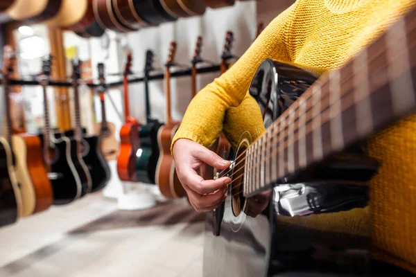 Jonge vrouw probeert en koopt een nieuwe houten gitaar in instrumentale of muzikale winkel, instrument concept — Stockfoto