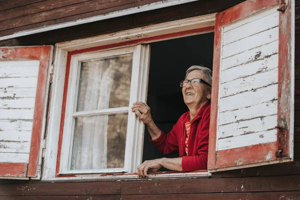 Веселая, улыбающаяся бабушка, смотрящая в окно и наслаждающаяся солнечным днем, пенсионной жизнью — стоковое фото