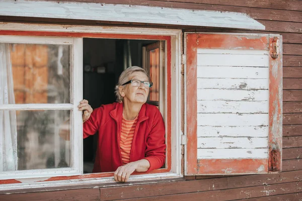 Retrato de una encantadora anciana o abuela mirando desde la ventana y sonriendo — Foto de Stock