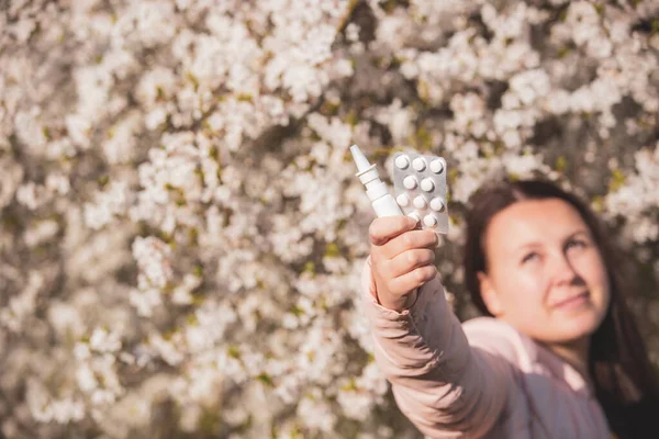 Allergi koncept, ung kvinna med piller eller droger och näsa eller nässpray mot den starka allergi i handen framför blommande ett träd under vårsäsongen, sjukvård — Stockfoto