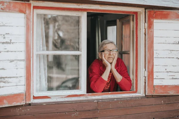 Портрет прекрасной пожилой женщины или бабушки, смотрящей из окна и улыбающейся — стоковое фото