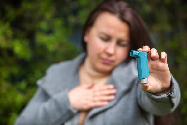 Mujer morena bastante joven teniendo un ataque de asma. Ella sostiene el inhalador. Mujer asmática usando un inhalador de asma durante los ataques de asma, concepto de salud — Foto de Stock