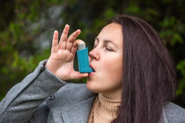 Pretty young brunette woman using an asthma inhaler during strong asthma attack, pharmaceutical product is used to prevent and treat wheezing and shortness of breath, healthcare concept