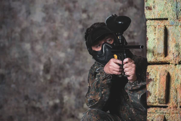 Ung man spelar paintball battle spel med sina vänner, bär kamouflage och skyddande mask, banderoll, fritidsaktivitet — Stockfoto