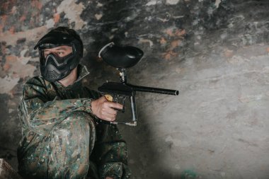 Profesyonel ekipman, maske, silah ve koruyucu miğfer ile paintball oynayan genç adam, birbirlerine boya kapsülleri atmak için hava tabancaları kullanarak askeri savaş simülasyonu yapıyor.