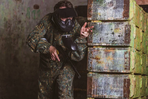 Ung man i paintball action med professionell utrustning, mask, pistol och skyddshjälm, simulera militär strid med luftgevär för att skjuta kapslar av färg på varandra — Stockfoto
