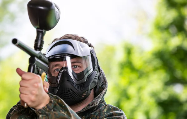 Porträtt av ung man med ansiktsmask och pistol i actionspel paintball, simulera militär strid med luftgevär för att skjuta kapslar av färg på varandra — Stockfoto