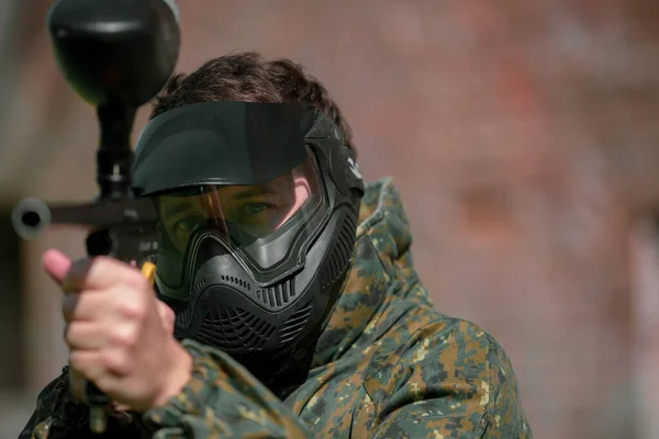 Porträtt av ung man med ansiktsmask och pistol i actionspel paintball, simulera militär strid med luftgevär för att skjuta kapslar av färg på varandra — Stockfoto