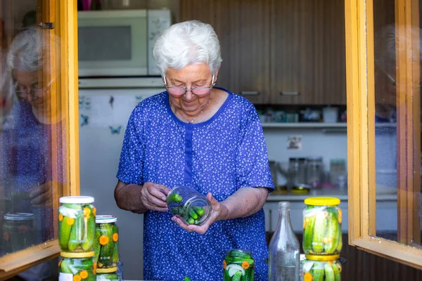 Mujer mayor o abuela hecho en casa enlatando los pepinos frescos, bio a un frasco con cebolla, zanahoria y eneldo, concepto de alimentos — Foto de Stock