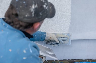 İnşaat işçisi dış bina duvarına taze sıva yapıştırıyor.