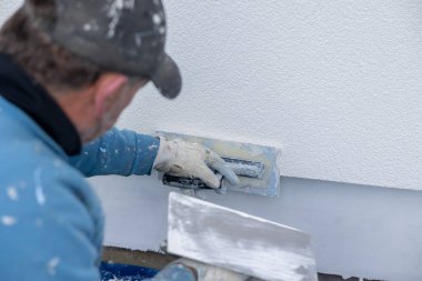 İnşaat işçisi dış duvara taze alçı uygulayıp dış görünüş dokusu yaratıyor.