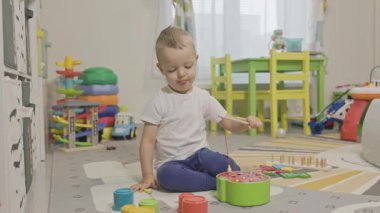 Evdeki halının üzerinde oturan genç bir çocuk renkli bir manyetik balıkçı oyuncağı oyunu oynuyor.