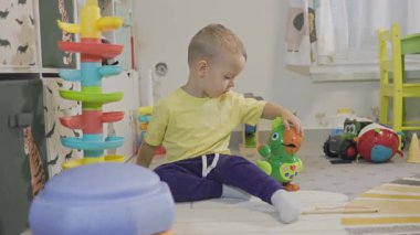 Genç çocuk odasında yerde oturmuş yeşil interaktif bir kuş oyuncağıyla oynuyor.