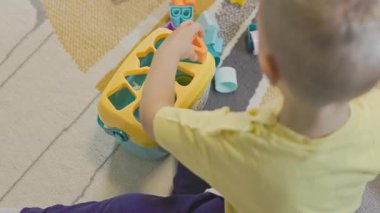 Yerde oturan küçük çocuk, güzel motor beceriler için sınıflandırıcı bir oyuncakla şekil ve renkleri öğreniyor.