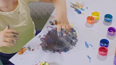 Sevimli, mutlu çocuk parmaklarıyla resim yapmayı seviyor, beyaz bir kağıt parçasında renkleri karıştırıyor.