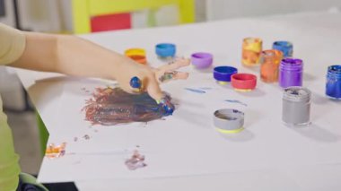 Okuldaki resim dersinde çocukların elleri beyaz kağıda renkli boyaları karıştırıyor.