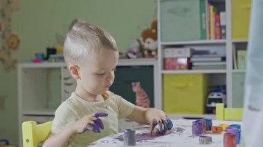 Ellerinde boya olan sevimli küçük çocuk masada renkli bir şaheser yaratıyor.