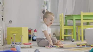 Tatlı çocuk yerde otururken renkli bir oyuncak ksilofon çalmayı öğreniyor.