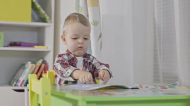Yoğunlaşmış küçük çocuk bir masada oturmuş güzel motor beceriler geliştiren bir kitaba çıkartmalar yapıştırıyor.