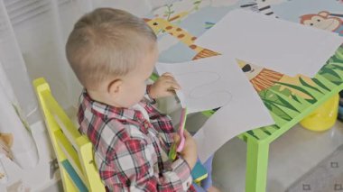 Kağıttan bir şekil kesmeye konsantre olan sevimli bir çocuk. Çocuk için güvenli bir makasla.