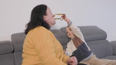 Sevimli küçük çocuk büyükannesinin gözlükleriyle oynuyor, kanepede keyifli bir anı paylaşıyor.