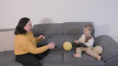 Neşeli büyükannesi ve torunu kanepede balonlarla oynayarak eğleniyorlar.