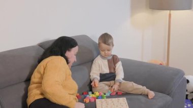 Genç oğlu ve annesi oturma odasındaki kanepede tahta harflerle oynuyorlar.