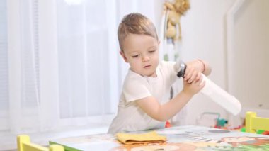 Sevimli çocuk, oyun odasındaki renkli masasını spreyleyip silerek ev işlerini öğreniyor.