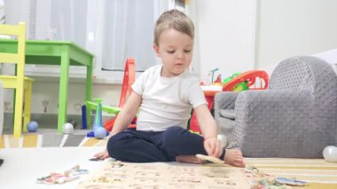 Küçük çocuk odasında yerde oturmuş, ahşap bir bulmacayı çözmeye çalışıyor.