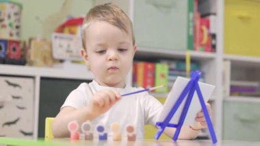 Odasında küçük bir tuval sehpasında fırçayla resim yapan tatlı bir çocuk.