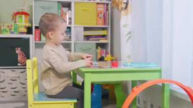 Masada oturan ve odasındaki renkli mankenlik kiriyle oynayan sevimli küçük çocuk.