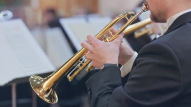 Bir senfoni orkestrası performansı sırasında trompet çalan profesyonel bir müzisyenin yakın çekimi.