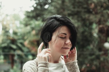 Kısa siyah saçlı kız Park 'ta kulaklıkla müzik dinliyor.