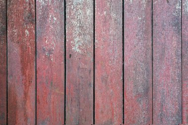 Dikey olarak sert tahtalardan yapılmış eski bir ahşap duvar. Kırmızımsı kahverengi boya kalıntıları ve ahşap malzemelerde oyuklar var. Geçmişi. Doku. 