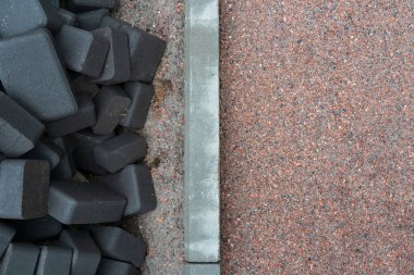 Hazırlanmış kaldırım sahasının en üst manzarası ve bir yığın siyah asfalt. Ortada kurulu bir kaldırım taşı var. Geçmişi. Doku. 