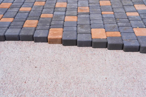 Gri ve sarı asfalt levhalar bir kum karışımının hazırlanmış yüzeyine konur. Döşeme kaldırımının kenarı görünür. Geçmişi. Kum ve çimento bloklarının dokusu. 