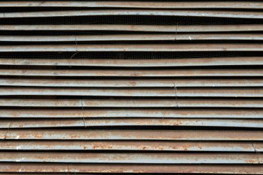 Eski bir endüstriyel havalandırma penceresinin yakın çekimi. Hoparlörün gri çelik elementleri kavisli ve yüzeyi aşınmış. Geçmişi. Doku. 