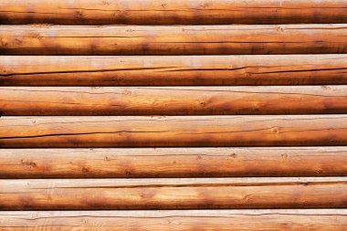 Aynı yuvarlak kahverengi kütüklerden yapılmış, kırsal ahşap bir evin duvarı. Yüzey koruyucu bir bileşikle tedavi ediliyor. Ormanda çatlaklar var. Geçmişi. Doku. 