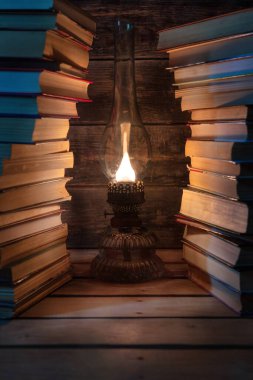Eski bir gaz lambası iki uzun kitap yığınının arasında parlar. Arkaplan. 