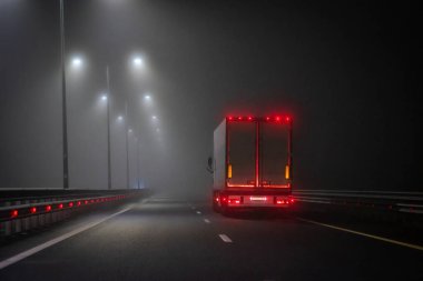 Kamyon siste gece yolu boyunca ilerliyor. Arka kırmızı ışıklar görünür. Sokak lambaları var..
